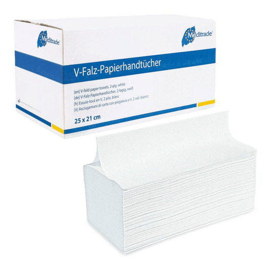 The image shows a box of folded paper towels with the inscription 'Meditrade Falthandtücher V-Falz 25x21cm 2-ply, white'. The predominantly white box with blue accents contains high-quality paper towels in the sizes 25 x 21 cm and with two-ply construction. In front of the box is a stack of these folded towels from Meditrade GmbH, which are perfect for hand hygiene.